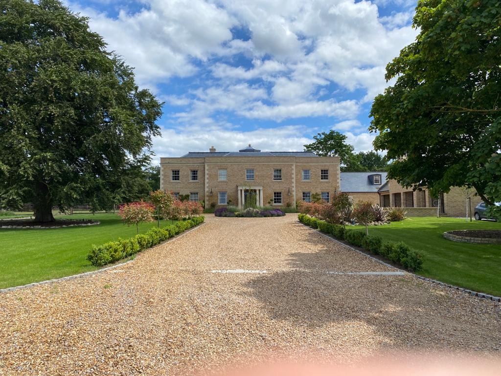 The finished classical country house with a sweeping gravel driveway and landscaped grounds by DNR Build