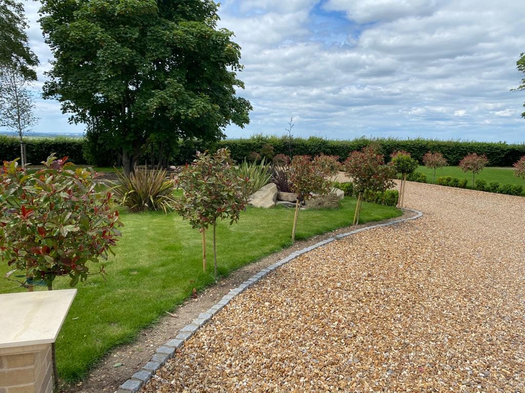 Planted garden borders and gravel paths in the landscaped grounds of the country house by DNR Build
