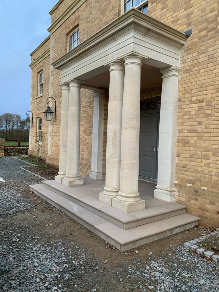 The completed natural stone portico with carved columns and stone steps at the front entrance by DNR Build