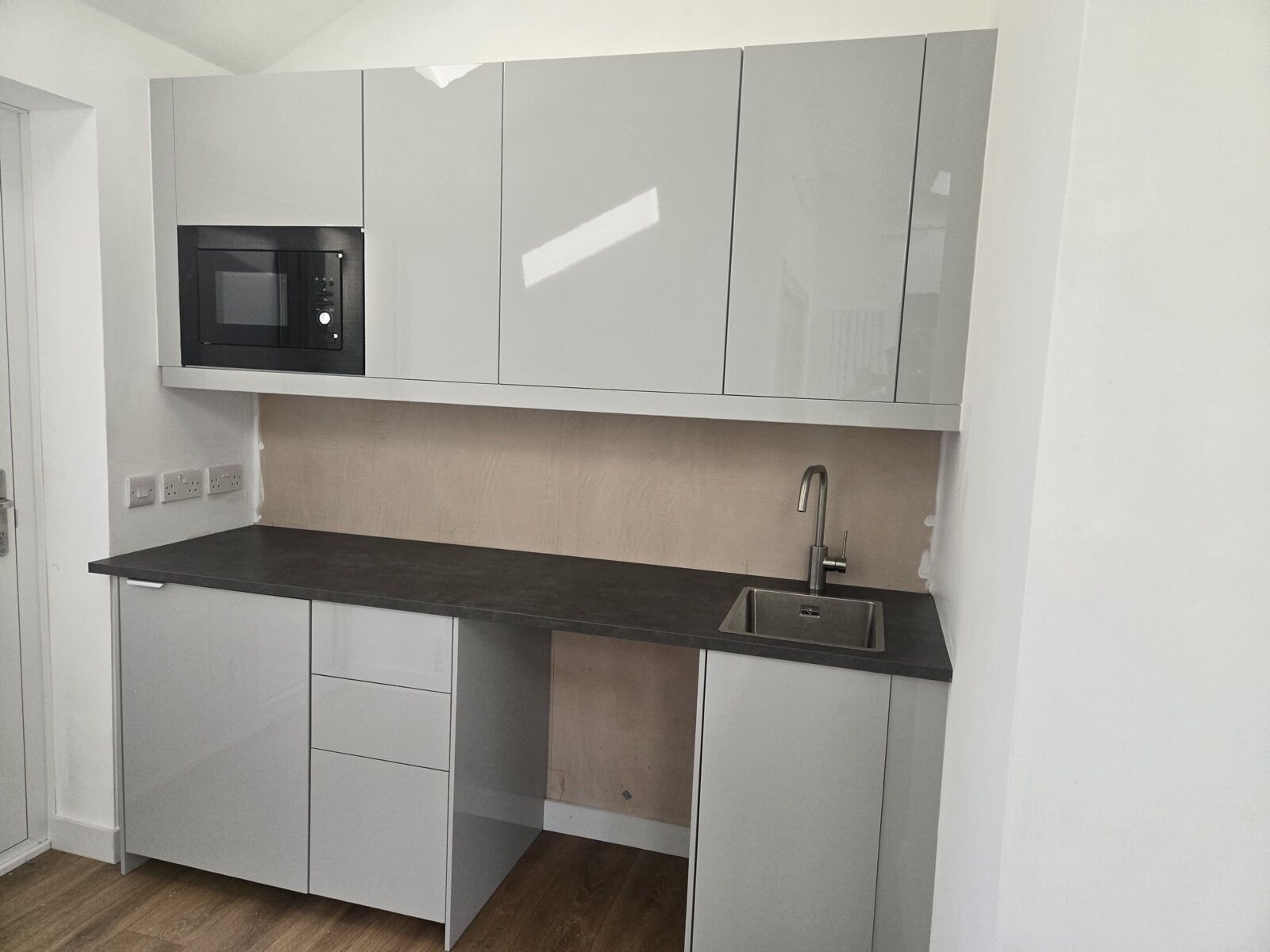 Finished annexe kitchenette with grey gloss units and a dark worktop by DNR Build