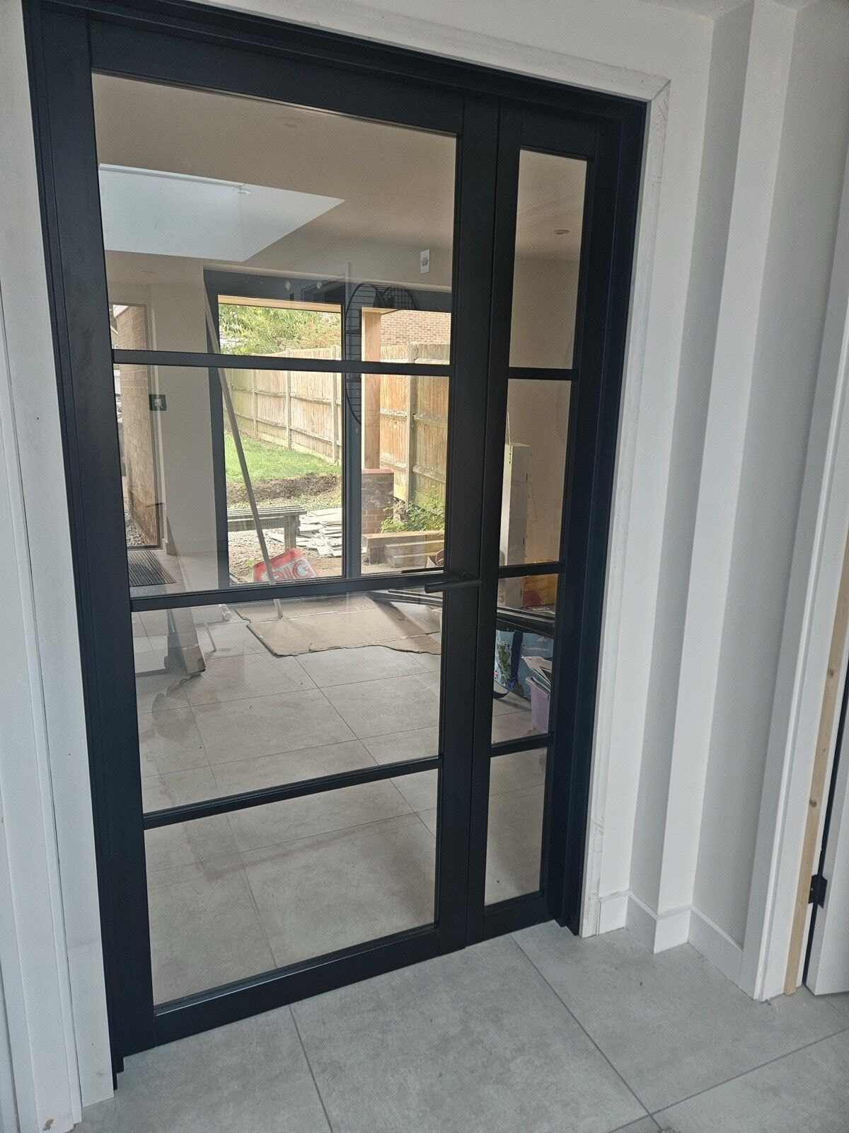 Black framed Crittall style glazed internal door looking through to the open plan living space and garden by DNR Build