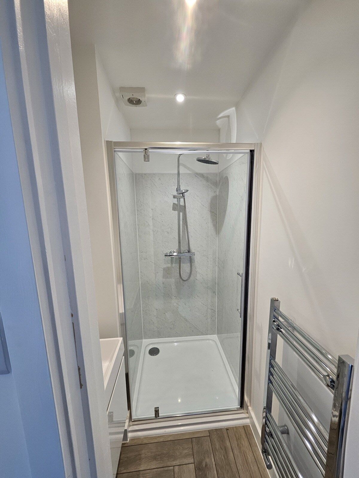 New shower room with a marble effect enclosure, glass screen and heated towel rail by DNR Build