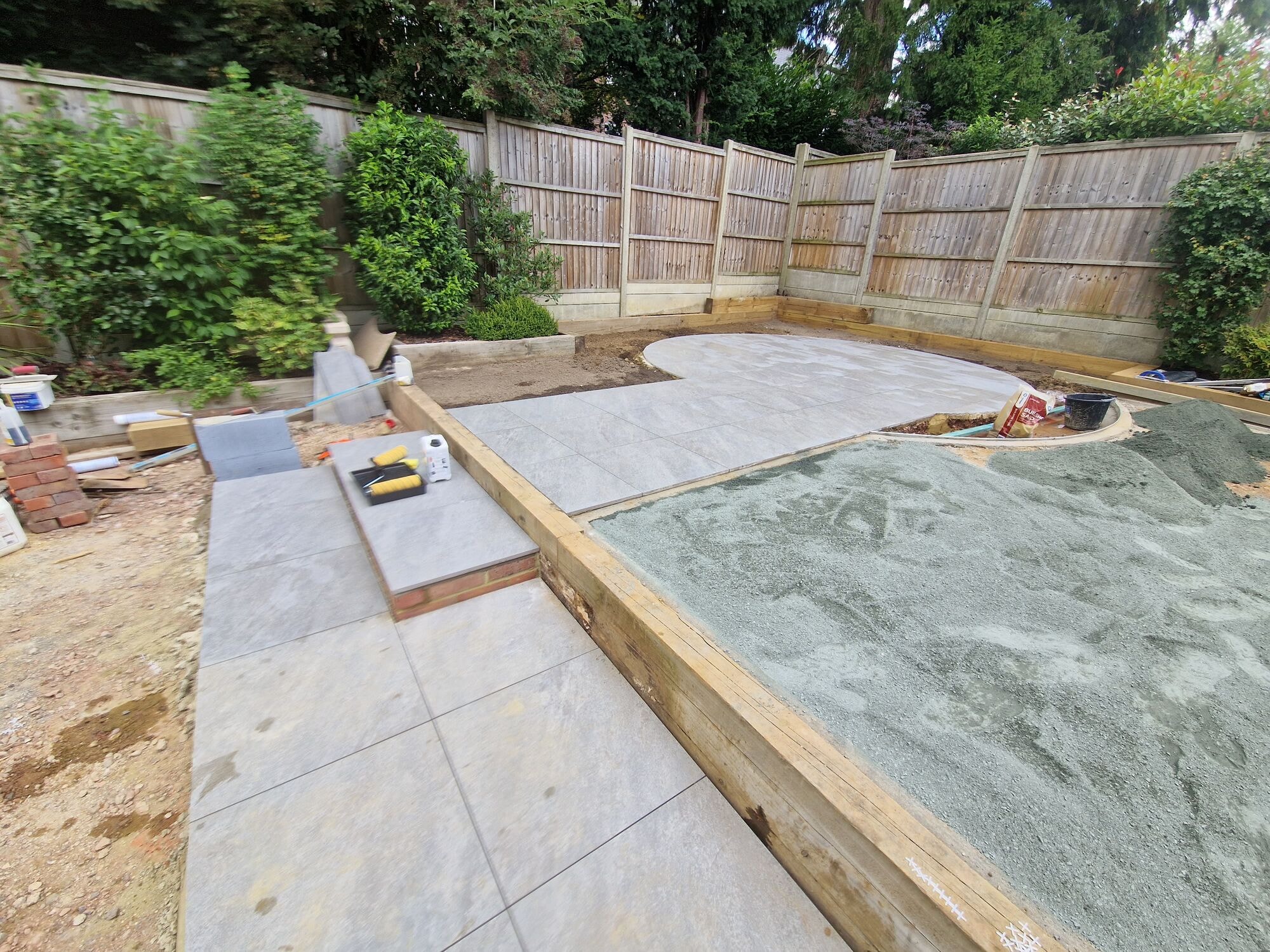The circular porcelain patio being laid on a prepared base with sleeper edging during the garden build by DNR Build