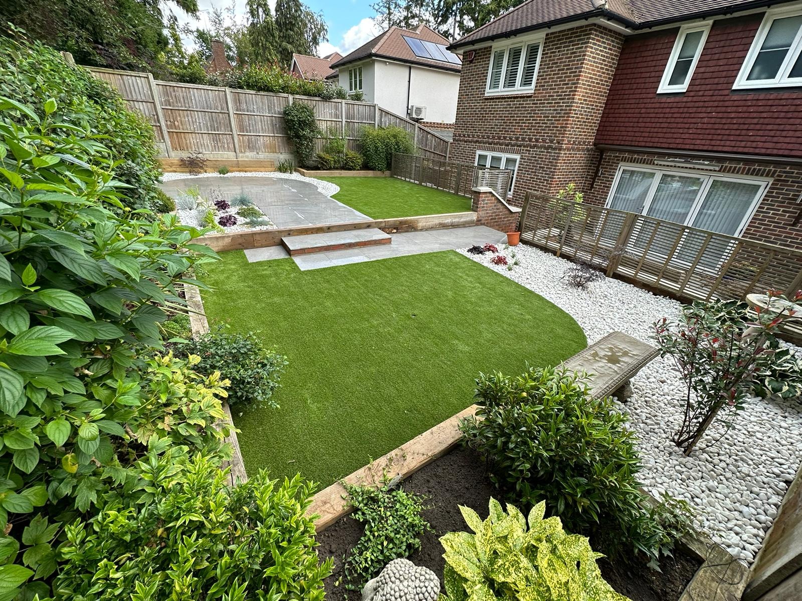 Elevated view of the finished garden with a circular porcelain patio, shaped lawn and pebble borders by DNR Build