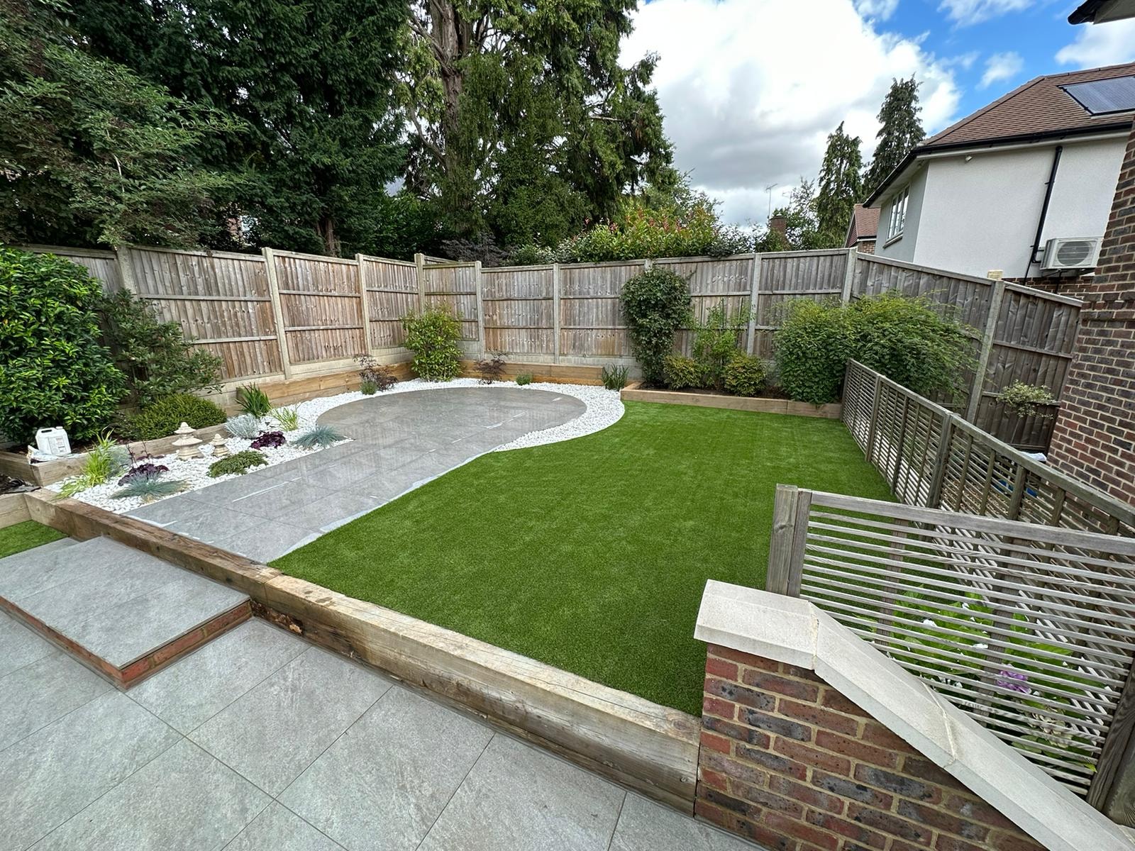 The finished shaped lawn and porcelain patio framed by sleeper raised beds and planting by DNR Build