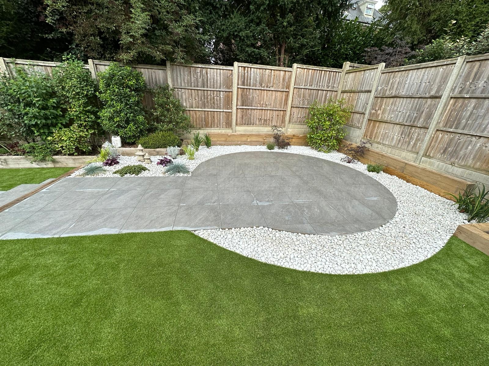 The circular porcelain patio with a white pebble surround and feature planting by DNR Build
