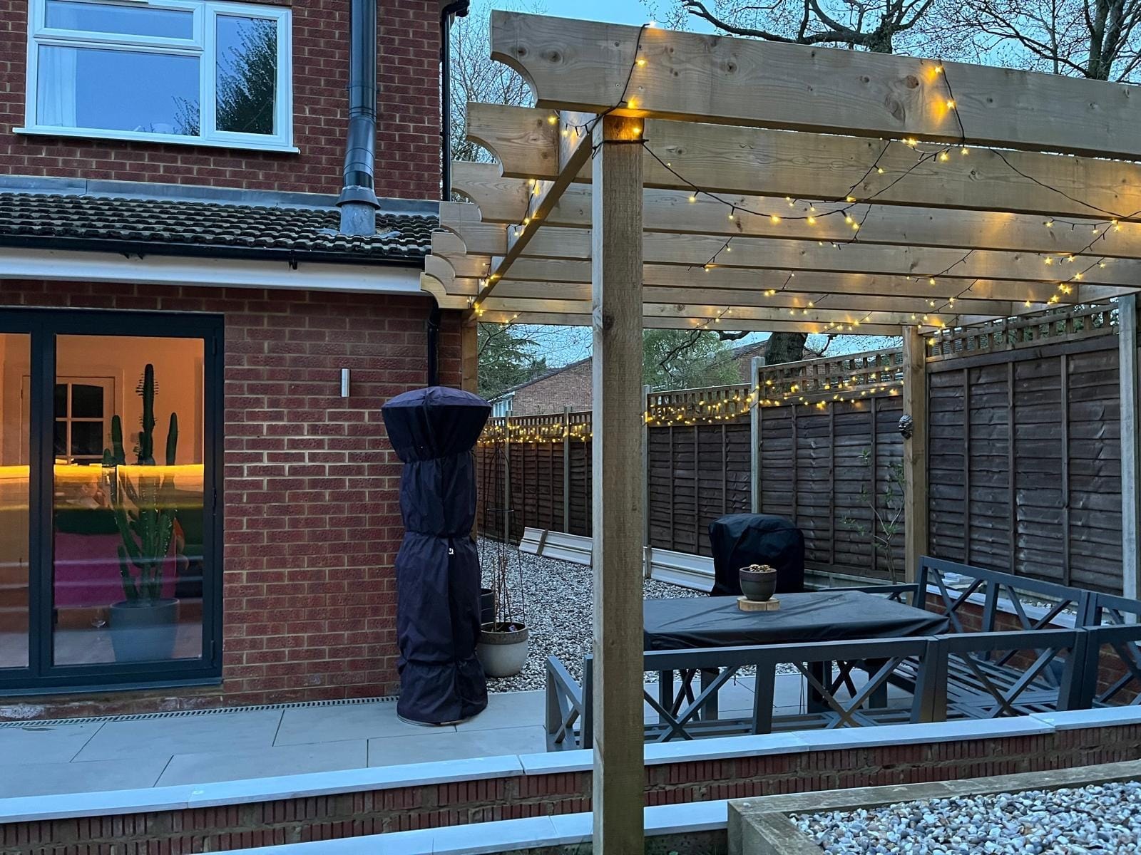 The rear of the house beside the timber pergola and seating area, with festoon lights along the fence by DNR Build