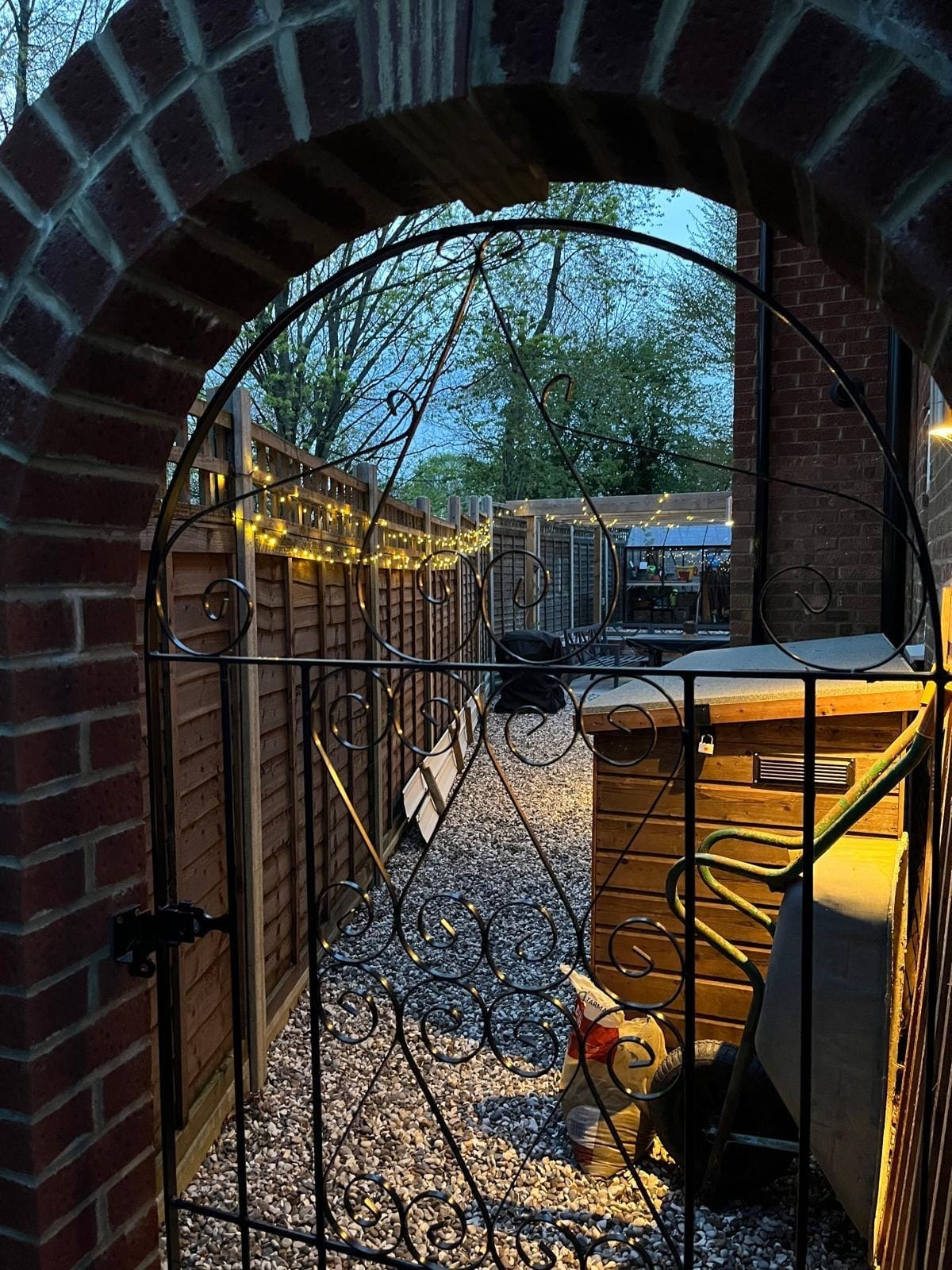 The brick archway and gate opening onto the gravel side path, with festoon lights along the fence by DNR Build