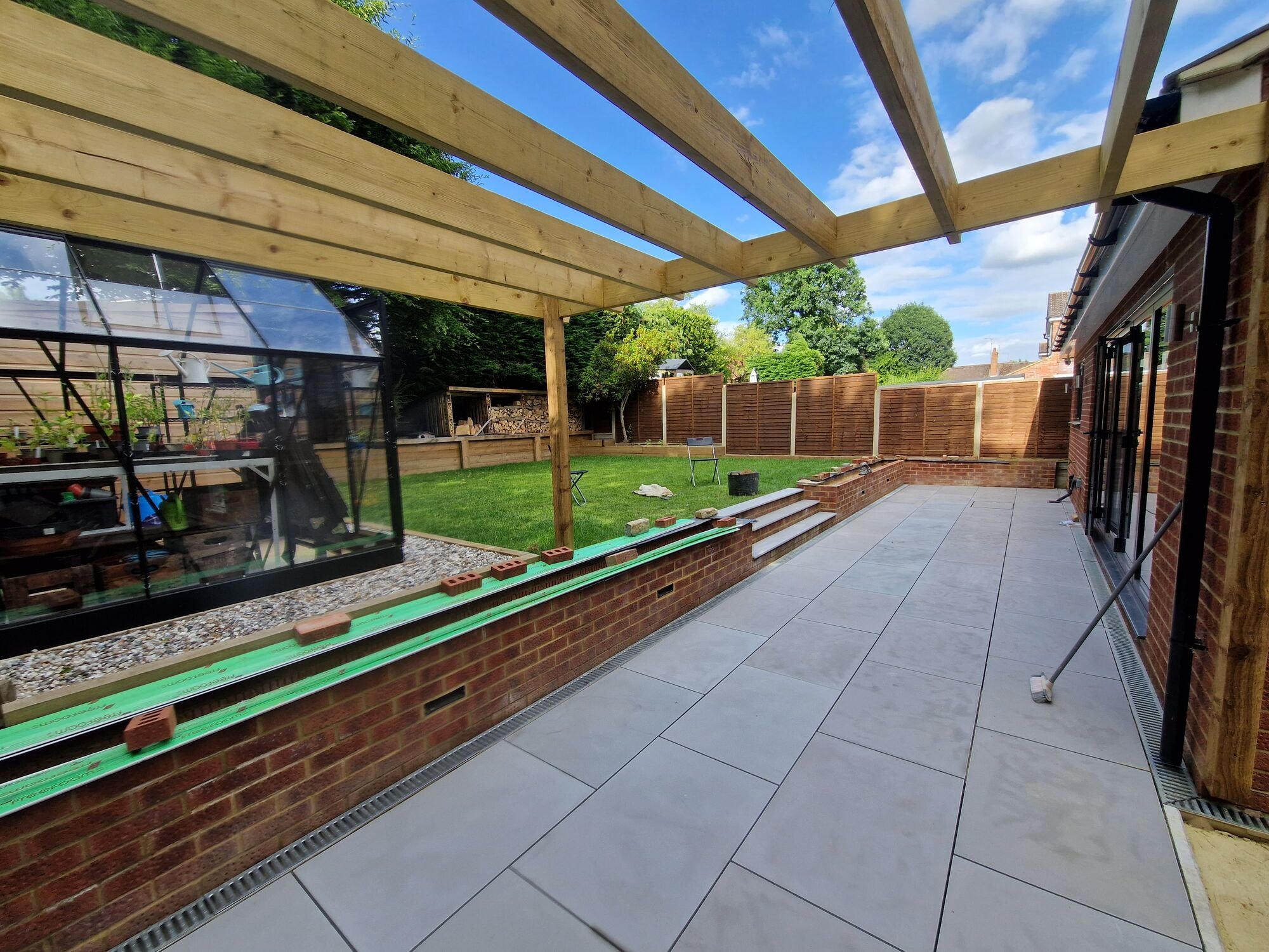 The finished garden with a timber pergola over the new porcelain patio, lawn and greenhouse by DNR Build