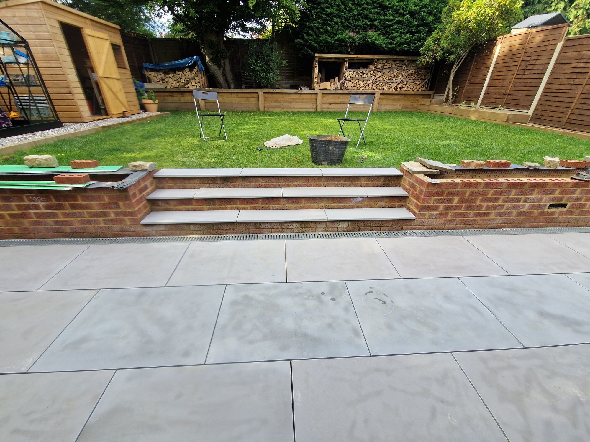 Porcelain steps up to the lawn with the shed and log stores beyond by DNR Build