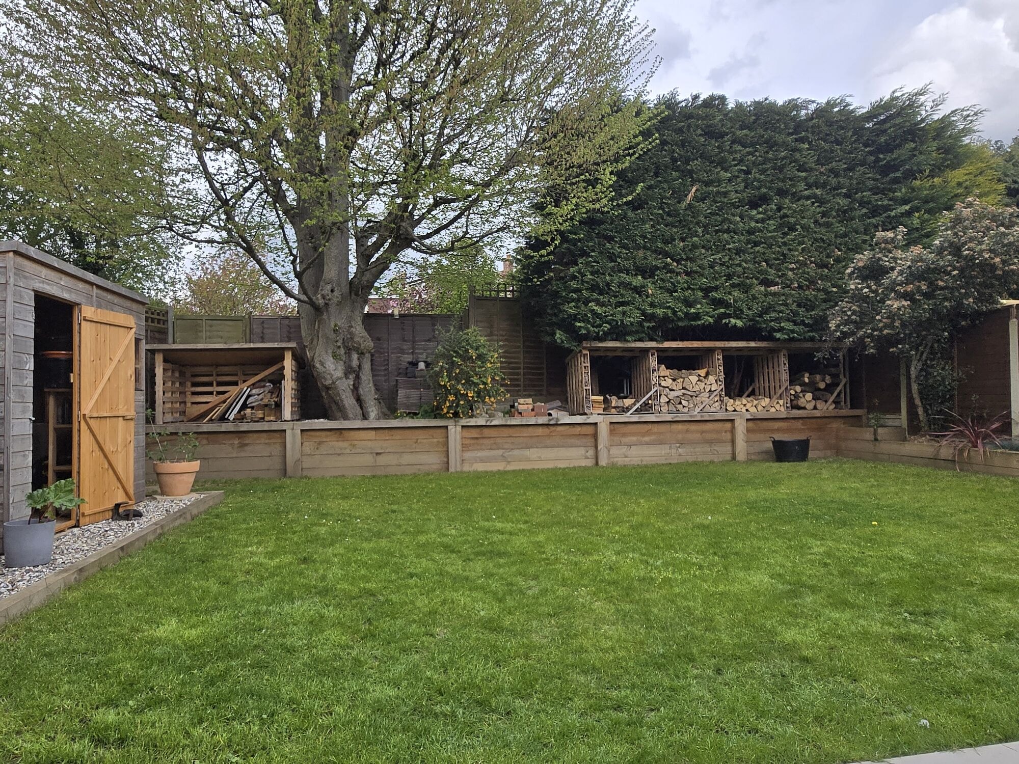 The mature garden with the lawn, sleeper raised beds, log stores and shed by DNR Build