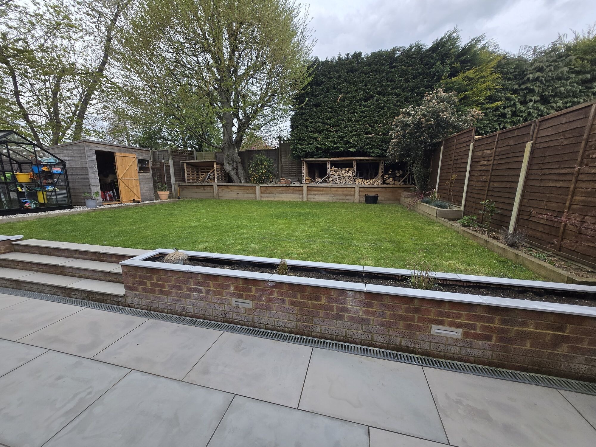 Wide view of the finished garden with the patio, brick retaining wall, lawn and trees by DNR Build