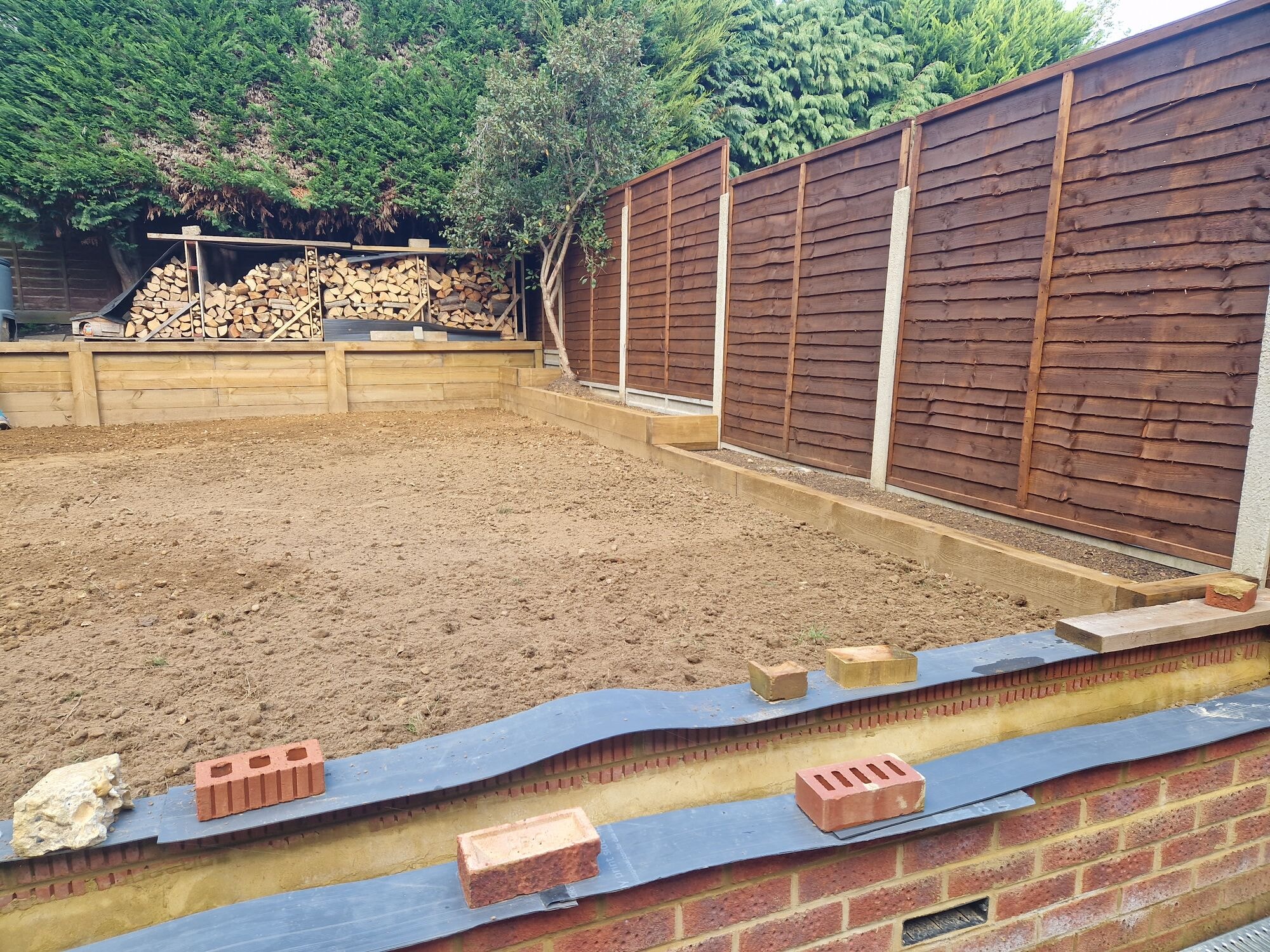 Sleeper raised beds in place and a new brick retaining wall being built with the ground levelled by DNR Build