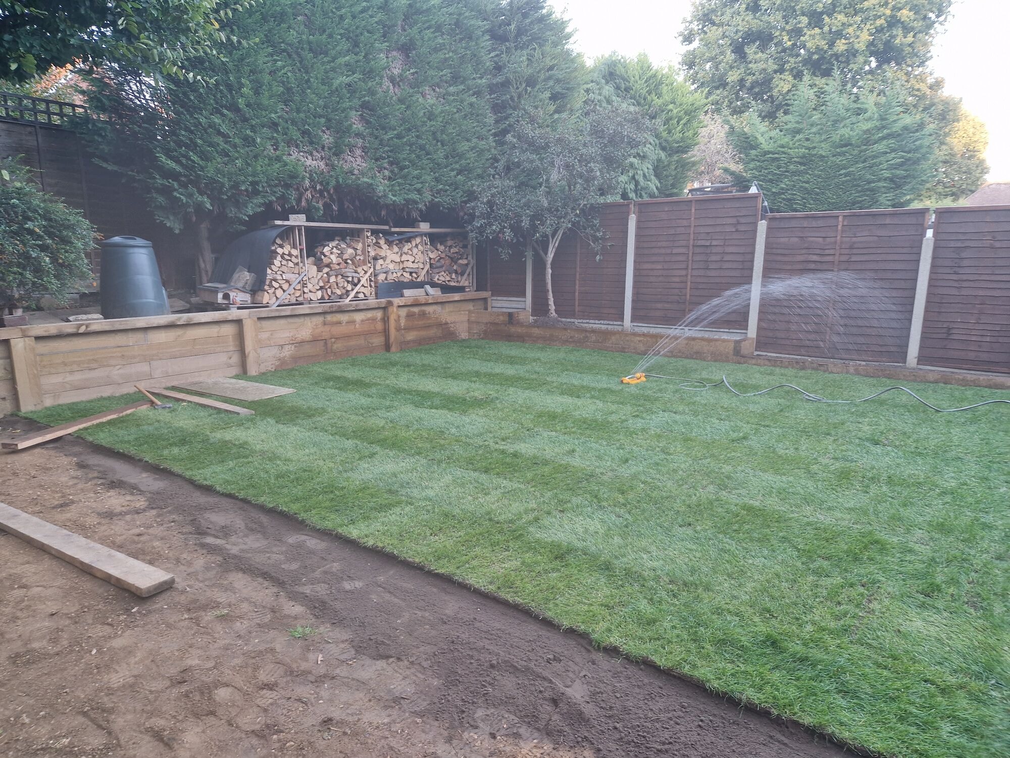 The finished new lawn laid and being watered, framed by sleeper raised beds and new fencing by DNR Build