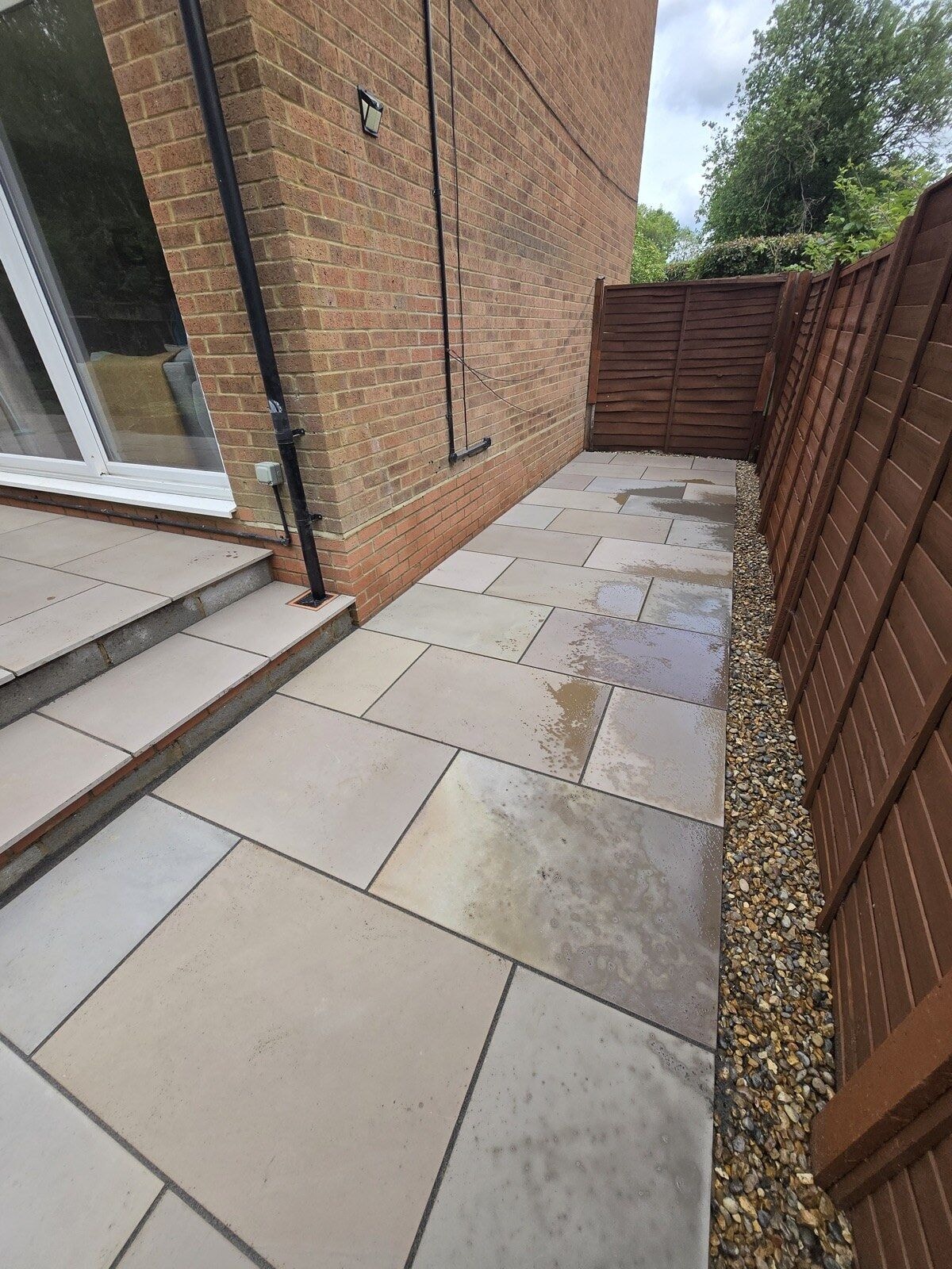 Sandstone patio running along the side return with a new gravel margin against the fence by DNR Build