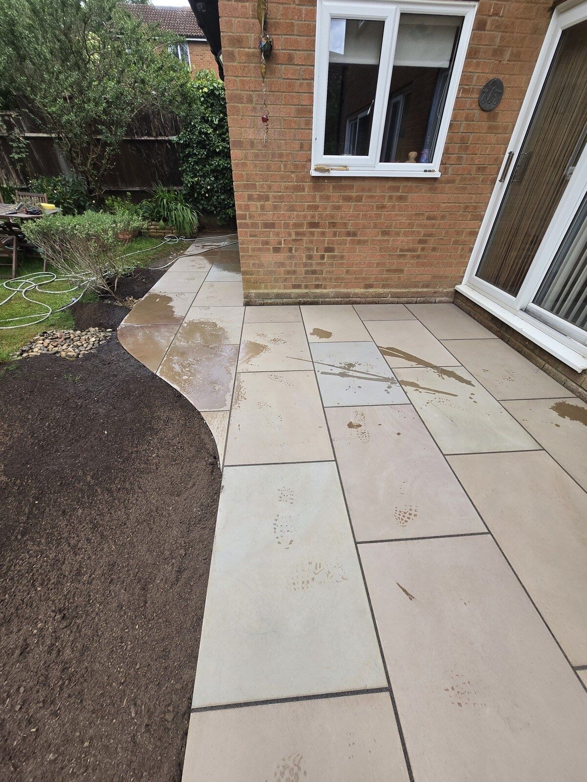 Sandstone patio sweeping around the house with a curved edge to the new lawn by DNR Build