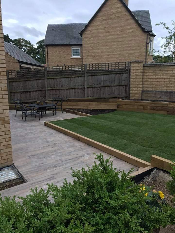 Porcelain plank patio with a dining set beside a level lawn and sleeper raised beds by DNR Build
