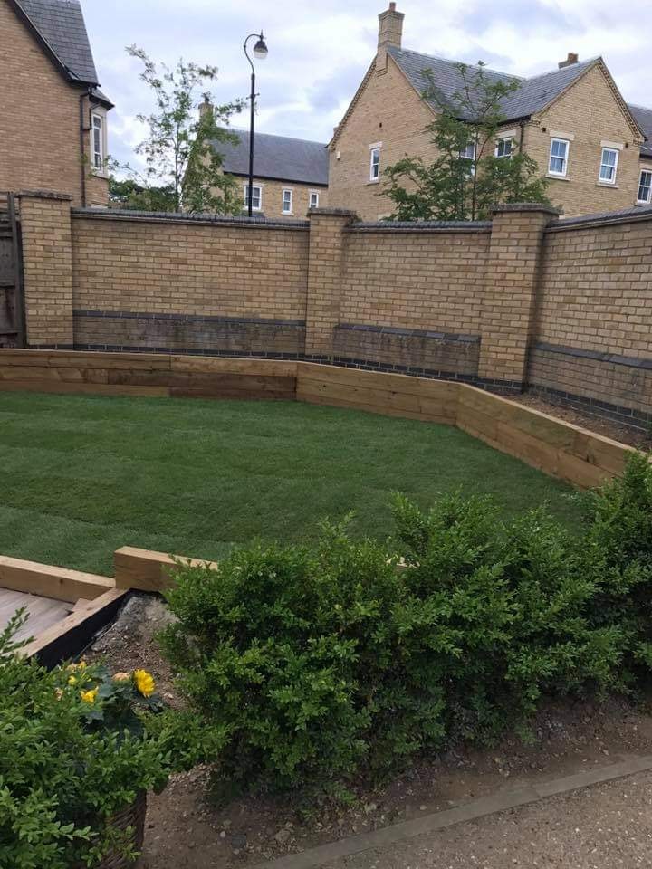 Level lawn framed by oak sleeper raised beds against a brick boundary wall by DNR Build