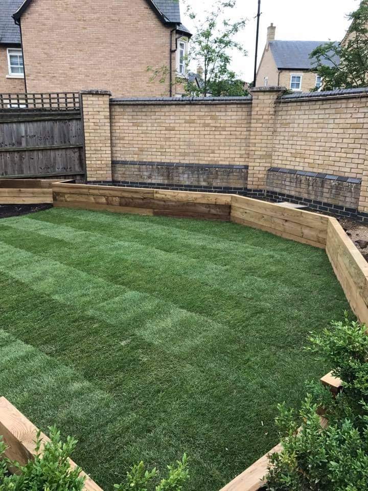 Striped lawn surrounded by sleeper edged raised beds and brick walls in the finished garden by DNR Build