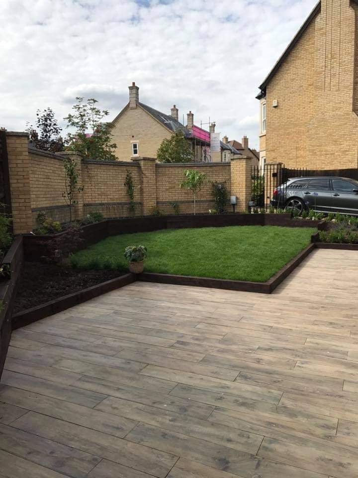 Porcelain plank patio sweeping round to a lawn, planted beds and the driveway by DNR Build