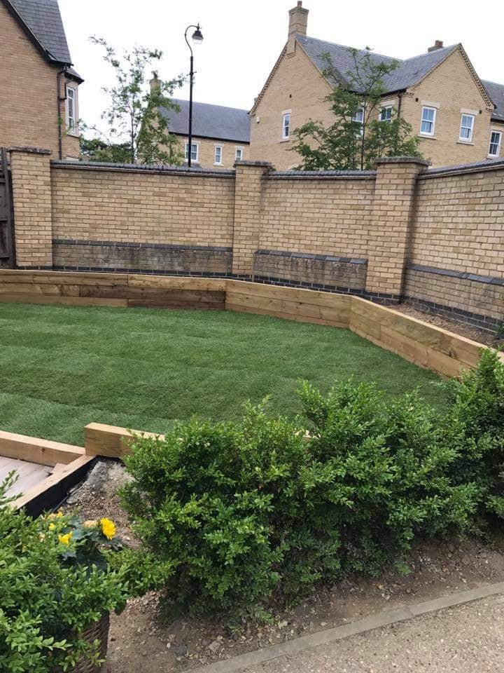 Level lawn framed by oak sleeper raised beds and a brick boundary wall in the finished garden by DNR Build