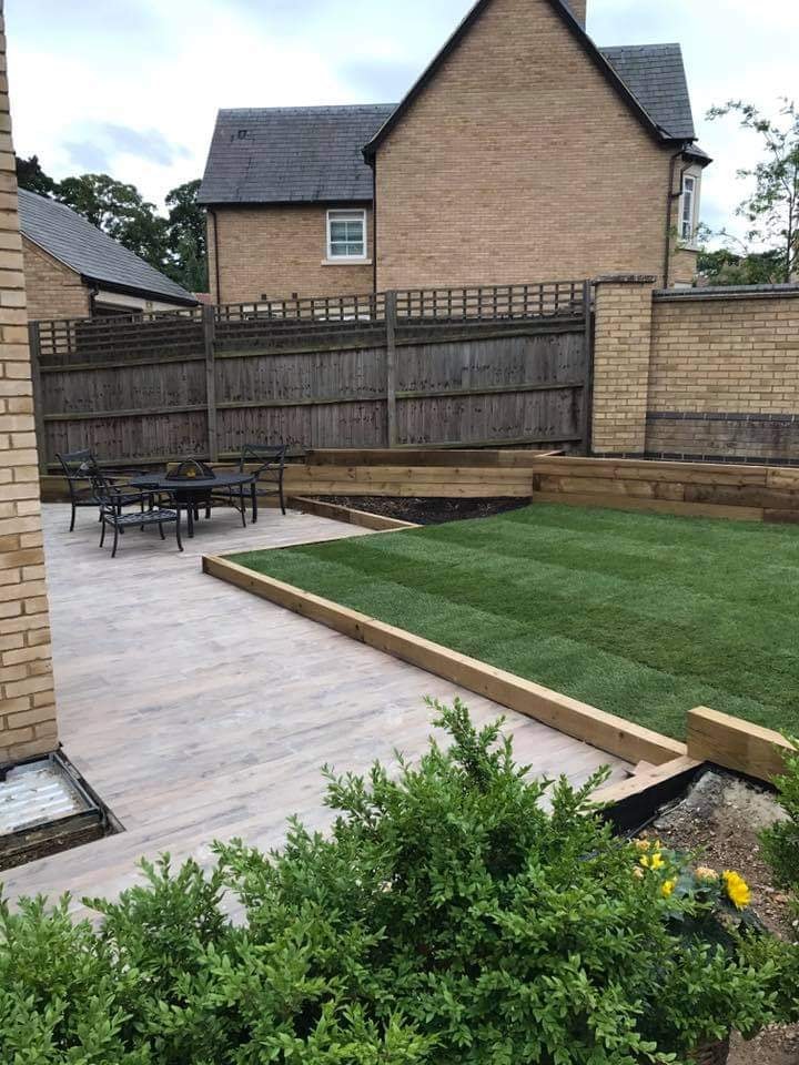 Porcelain plank patio with a dining set and fire pit beside the new lawn and sleeper raised beds by DNR Build
