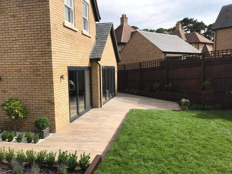 The side of the home with bi-fold doors opening onto a porcelain plank patio, lawn and lavender borders by DNR Build