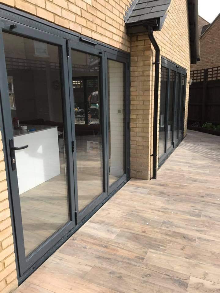 A run of bi-fold doors along the home opening onto the new porcelain plank patio by DNR Build