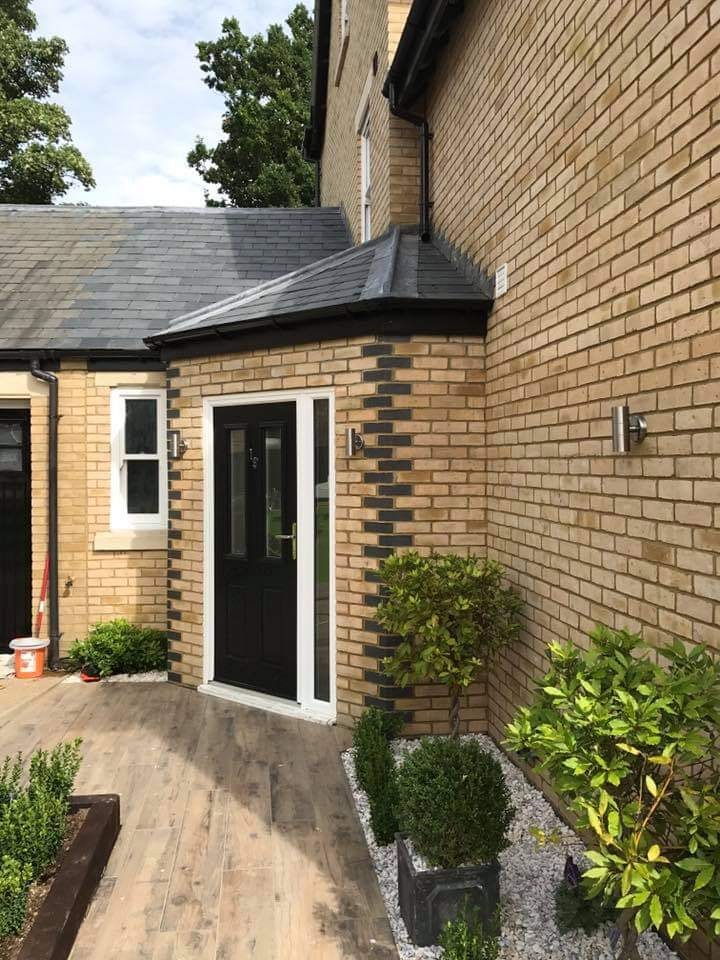 The entrance porch with a black composite door, plank paving and shaped planting by DNR Build