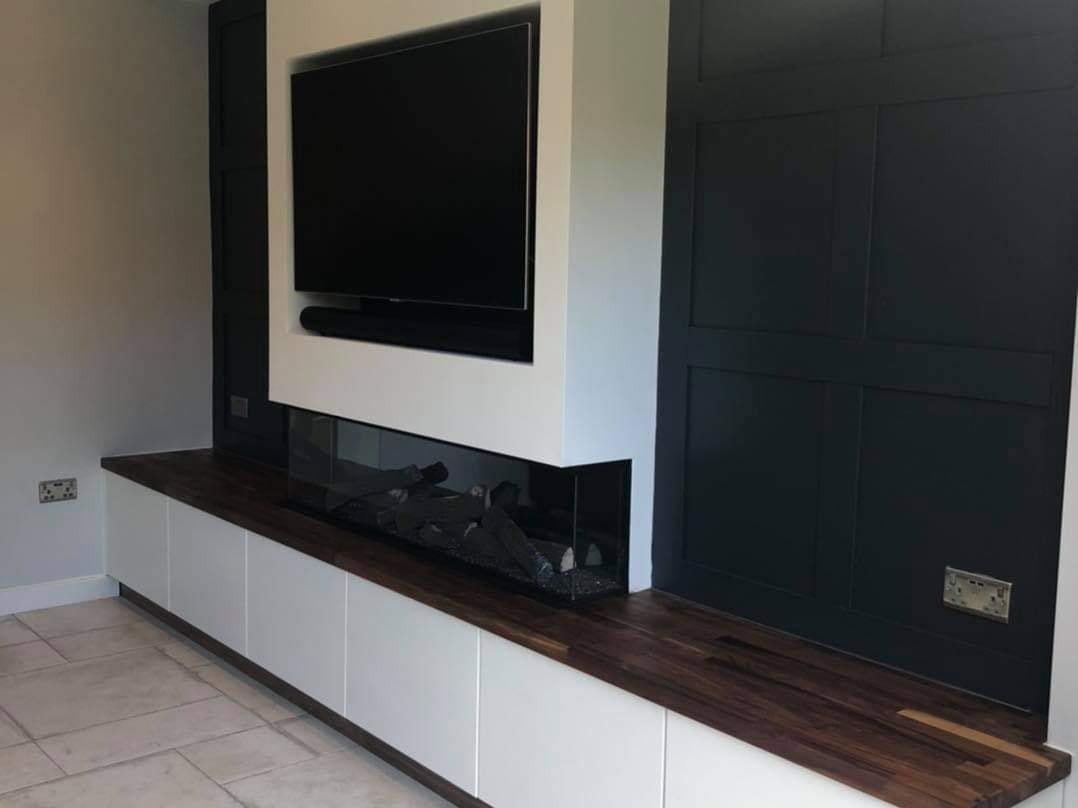Angled view of the panelled media wall with the inset fire, walnut worktop and handleless white cabinets by DNR Build